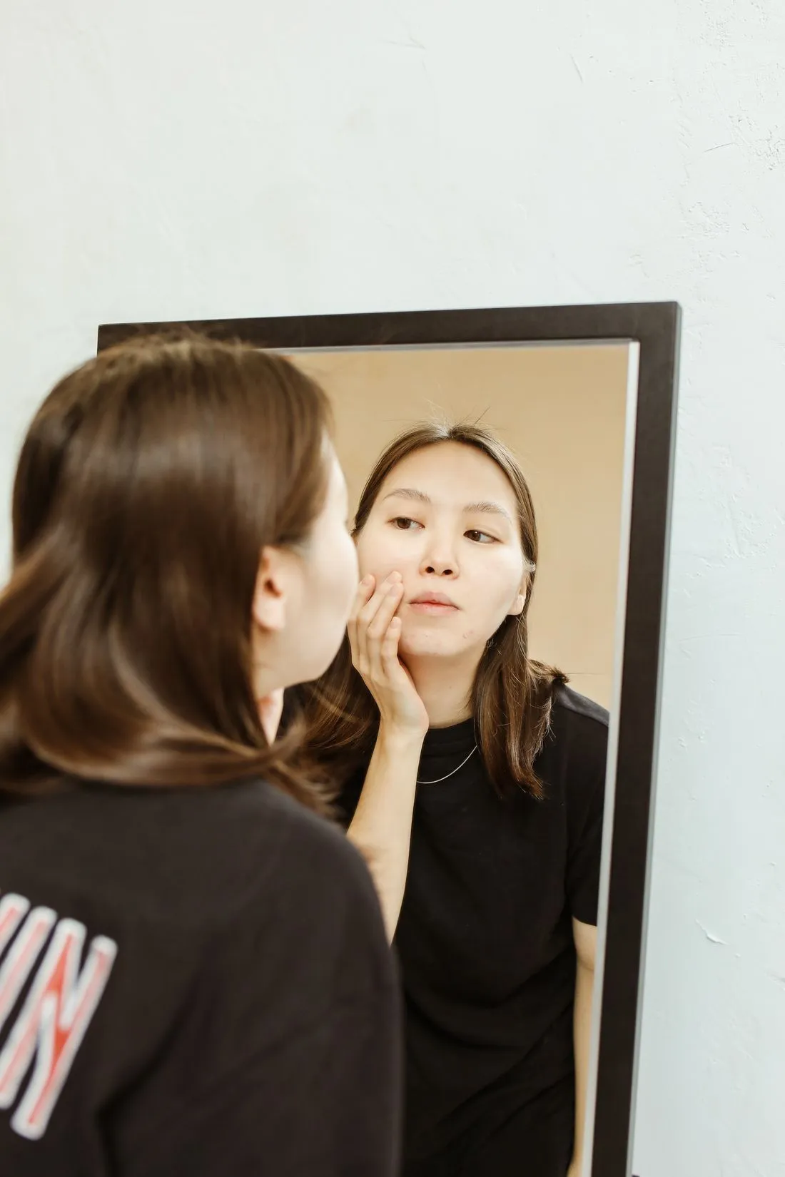 Neotonics Reviews 2 Woman examining her skin in a mirror, concerned about her complexion