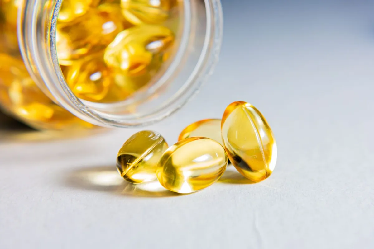 Golden omega-3 softgels spilling from a supplement jar